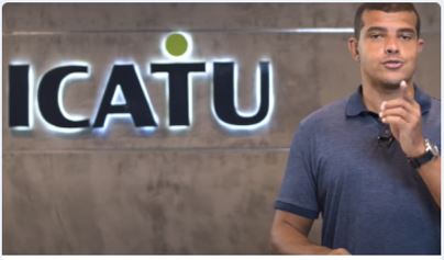 homem de camisa azul falando e gesticulando na frente de uma parede com o logo da empresa